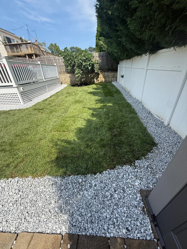 Finished lawn bordered by white decorative stone and a white fence