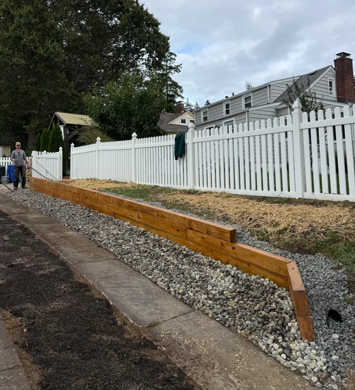 Timber retaining wall with gravel drainage beside a white fence