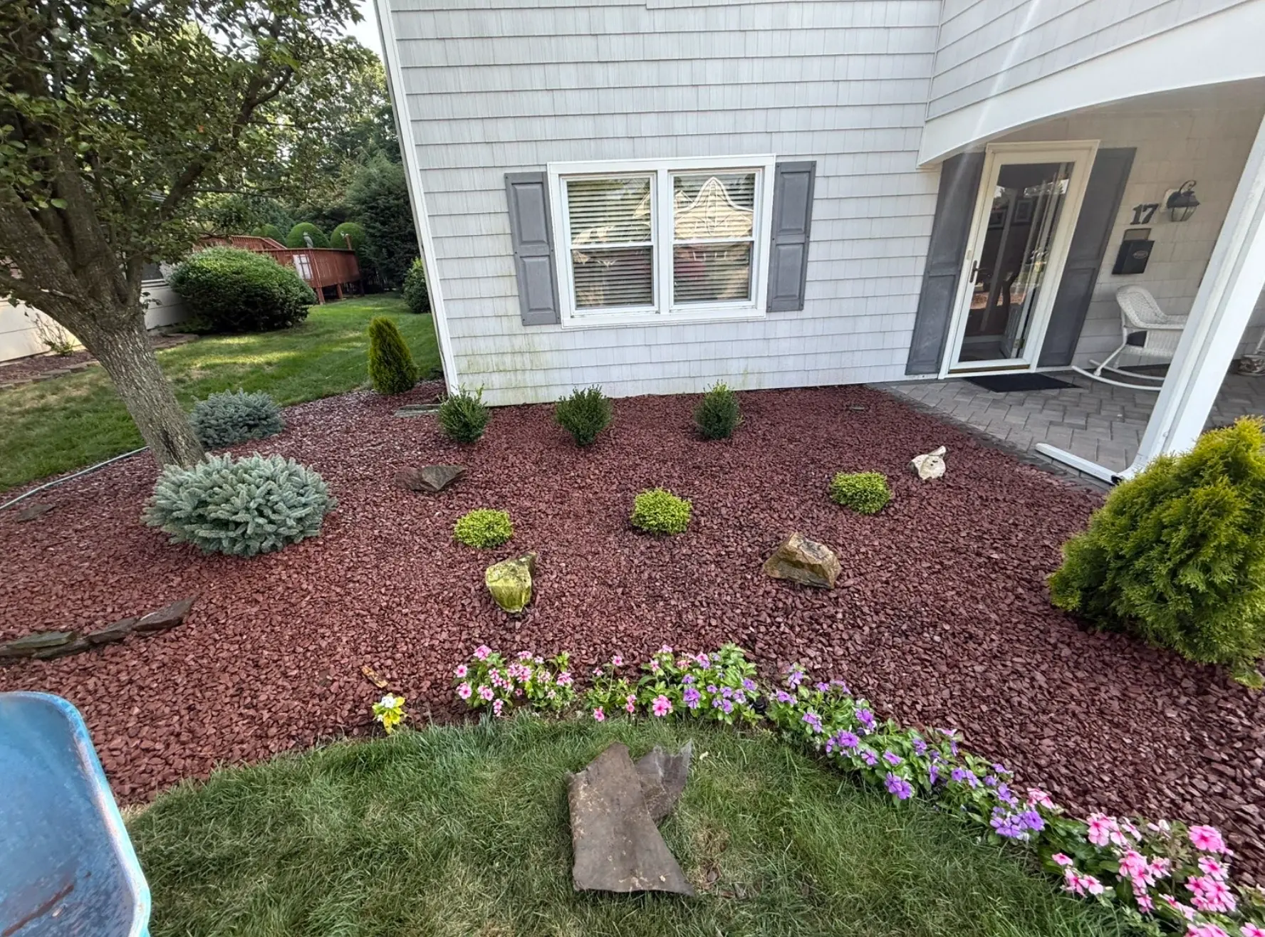 Colorful flower bed with red mulch, shrubs and stone accents in front of a home