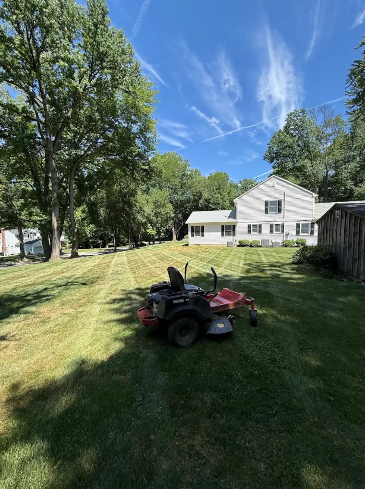 Large freshly mowed property with visible mowing lines and a riding mower