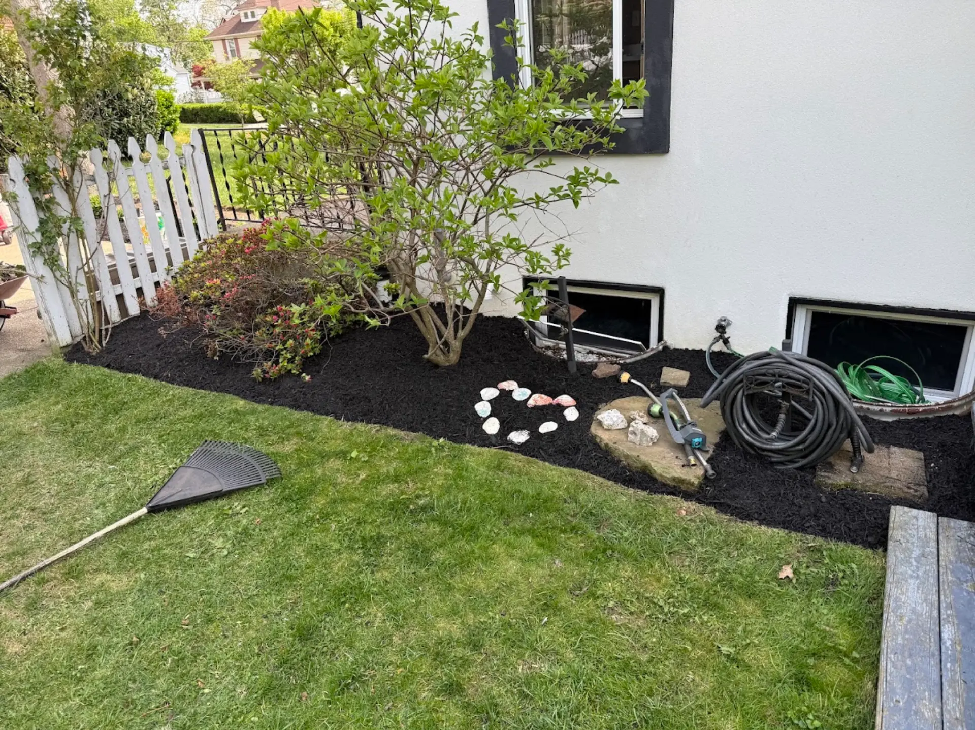 Freshly installed black mulch bed with shrubs and a crisp edge along the lawn