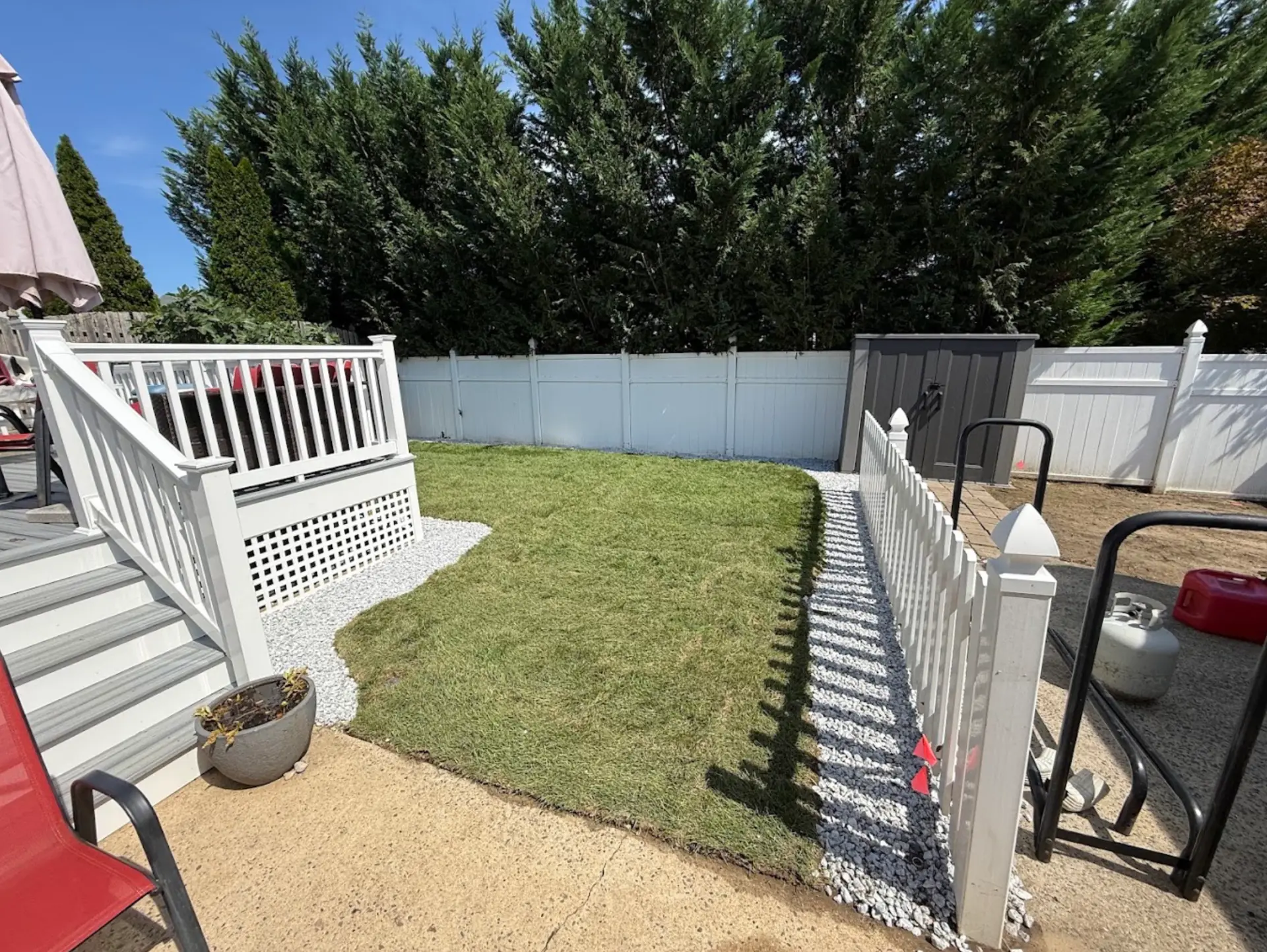 Completed backyard renovation with new lawn and white decorative stone around the deck and fence