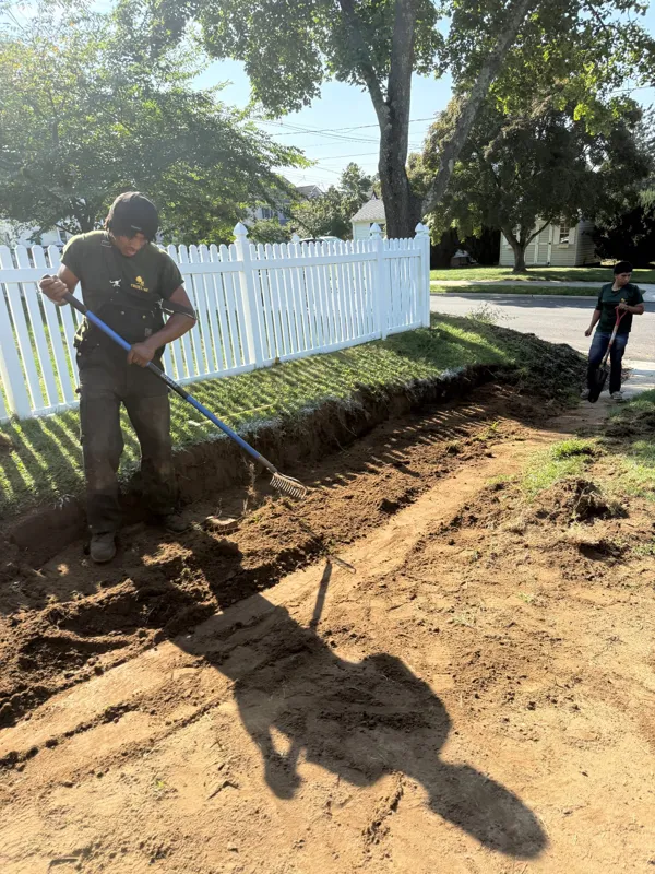 TrueLine crew raking soil along a fence to prepare a lawn