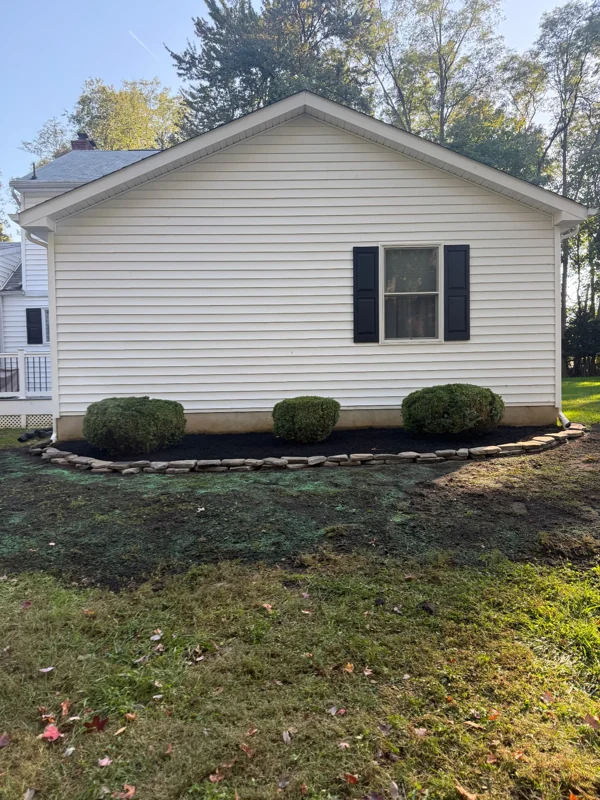 Trimmed shrubs in a stone-edged mulch bed along a home